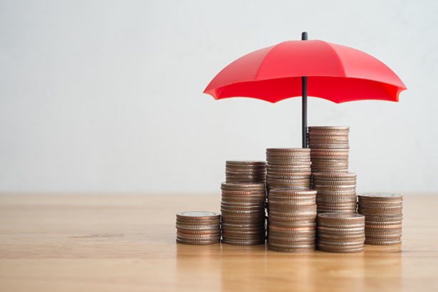 A photo of coins stacks on a table with a red umbrella over them.